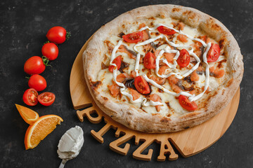 Homemade pizza with salmon. Cream sauce, mozzarella, salted salmon, tomatoes, cream cheese and orange zest on a dark background. Top view, side view