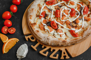 Homemade pizza with salmon. Cream sauce, mozzarella, salted salmon, tomatoes, cream cheese and orange zest on a dark background. Top view, side view