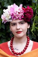 Girl brunette with red lips and a wreath of peonies on his head in the ethnic image of Mexican artist Frida Kahlo
