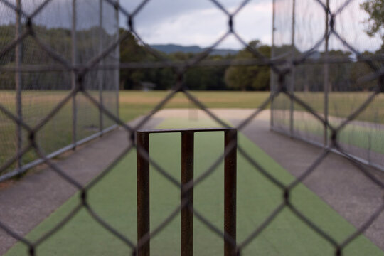 Cricket stumps and wicket viewed through a chainlink fence