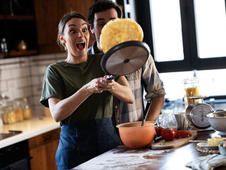 Husband and wife making pancakes at home. Young couple having fun in the kitchen.