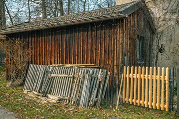 Stücke eines alten und des neuen Holzzauns vor einer Hütte aus Holz vor Bäumen im Frühjahr