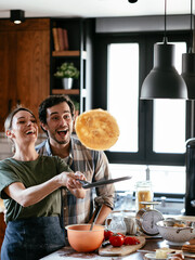 Husband and wife making pancakes at home. Young couple having fun in the kitchen.