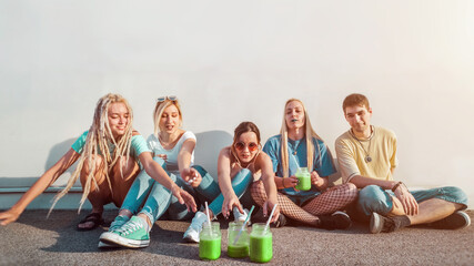 Group of young people reaching for green fruit smoothies, healthy drinks concept, youth and friendship