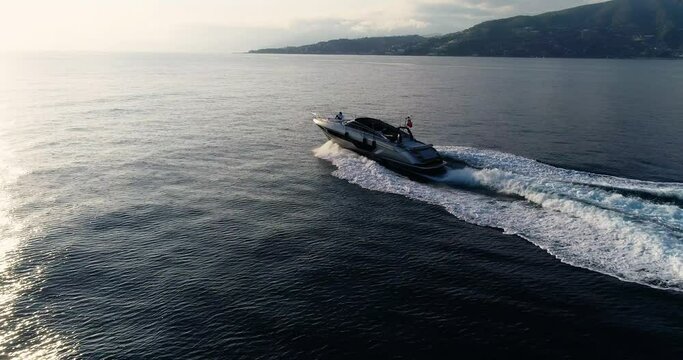 Aerial view with a drone of a yacht sailing at full speed under the sunset, with a man sitting in the front of the boat 4K