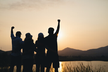 group of people with raised arms looking at sunrise on the mountain background. Happiness, success,...