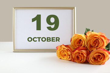 day of the month 19 October calendar photo frame and yellow rose on a white table