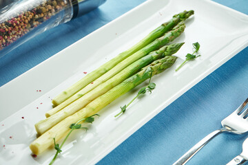 Delicious side dish for main courses - boiled asparagus with microgreen in a white plate on a blue...