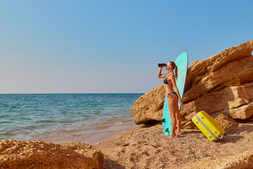 Cute woman with suitcase on seashore. Girl looking away through binoculars. New horizons, new life and future concept