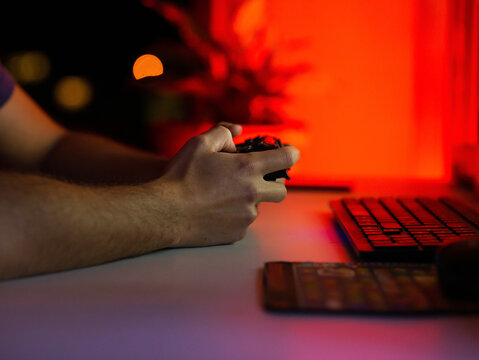 Crop unrecognizable male gamer using gamepad and playing video game while sitting at table with computer in dark room
