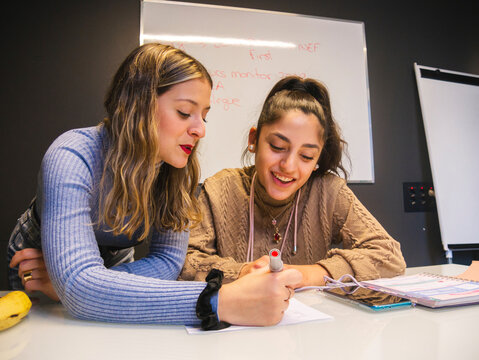 Student with marker explaining information for smiling classmate while working on homework assignment together against whiteboard