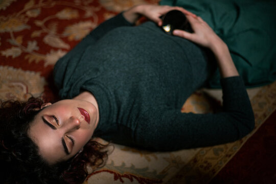 From above view of relaxed female with black hair lying on carpet with closed eyes and holding transparent crystal ball in room with retro design