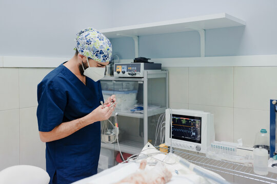 Unrecognizable male vet surgeon in uniform standing with cables from ECG monitor near table with cat before operation in hospital