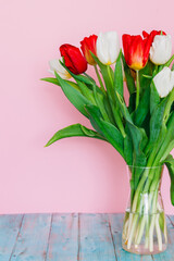 Beautiful spring red and white tulips in a vase on a table on a light pink background. Place for text