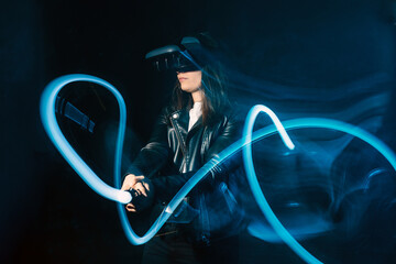 Side view of unrecognizable female wearing modern VR headset and playing with motion game controller in blue neon lights while exploring cyberspace