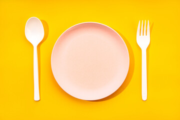 Top view composition with white plastic spoon and fork arranged near empty plate on yellow background