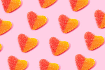Top view flat lay composition of multicolored jelly candies in shape of heart arranged in rows on pink background