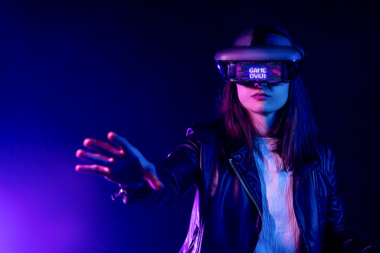 Unrecognizable female with outstretched arm wearing VR headset while exploring virtual reality under blue neon light near wall with projector illumination