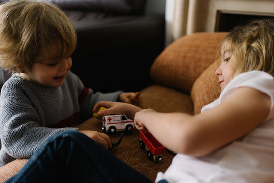 Side view of cute happy little sister and brother playing with toy cars while having fun together at home