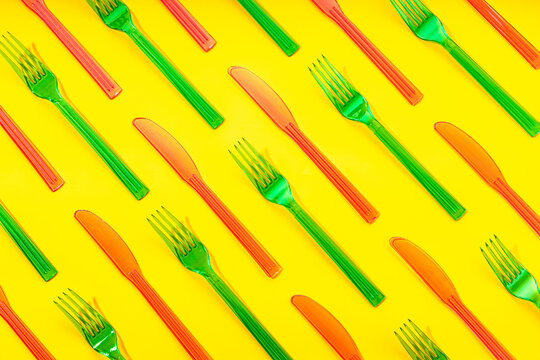 Top view full frame of colorful disposable plastic forks and knives arranged in order on yellow background