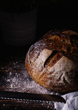 Delicious bread with crust covered in flour placed on napkin near knife on wooden table in bakery