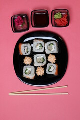 Rose in small bowl, marinated ginger and wasabi, rice roll with salmon and chopsticks on pink background