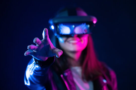 Unrecognizable female with outstretched arm wearing VR headset while exploring virtual reality under blue neon light