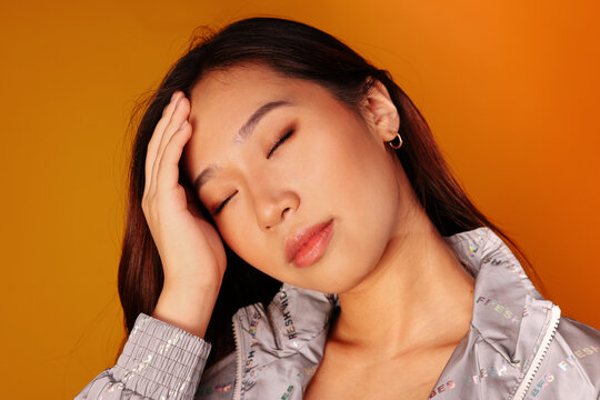 Worried chinese young woman with eyes closed over yellow background