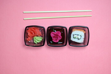 Rose in small bowl, marinated ginger and wasabi, rice roll with salmon and chopsticks on pink background