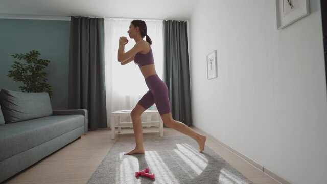 Active young lady doing squats exercises during domestic workout. Pretty woman leading active and healthy lifestyle. Concept of sport activity.
