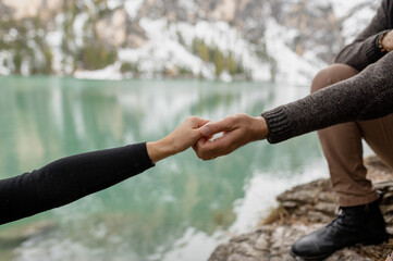 Crop anonymous traveler holding hand with girlfriend while supporting for climbing on rocky shore of Lago di Braies lake in Italy