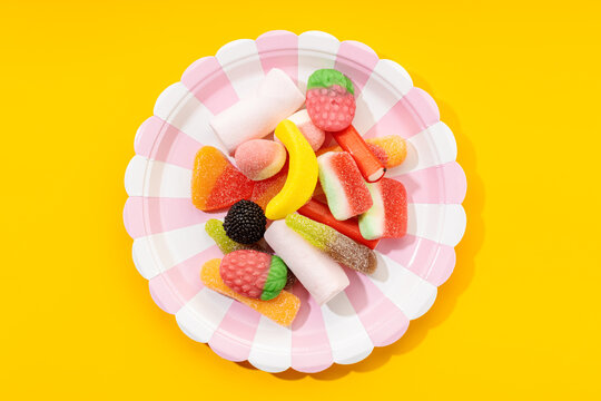 Top view of yummy multicolored gummy candies on striped plate placed on yellow background