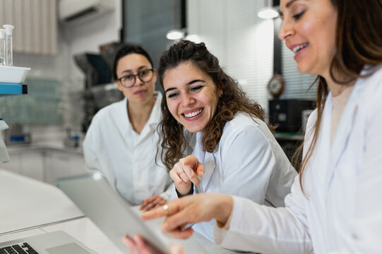Young female pharmacy researchers gathering at table with laptop with diagrams and discussing results of research while working together in scientific lab