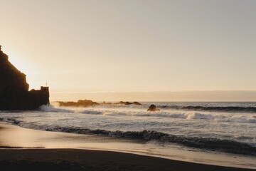 Picturesque view of sea waves rolling on sandy beach with rocky cliffs against sunset sky on Tenerife island in Spain
