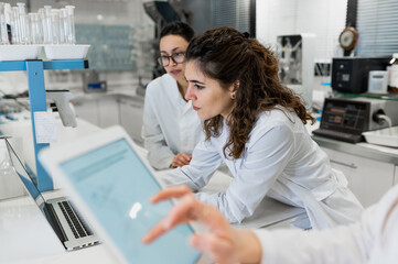 Young female pharmacy researchers gathering at table with laptop with diagrams and discussing results of research while working together in scientific lab