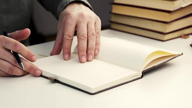 Male hand opening notebook and writing with pen.