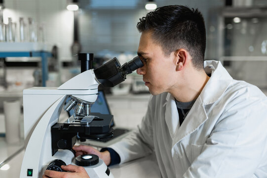 Side view of skilled male scientist using microscope while conducting chemical experiment in modern lab