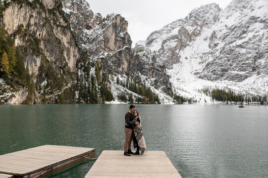 Full body of loving gentle couple hugging each other on wooden pier against Lago di Braies lake surrounded by snowy mountains