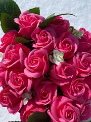 Bouquet of pink roses with green leaves on the snow background. 	