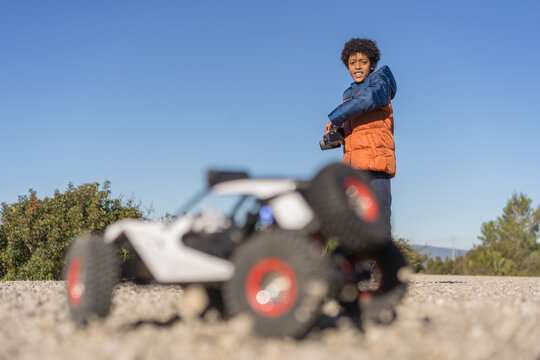 Cute Afro Kid With Curly Hair Operating Radio Controlled Car In The Park. Car Out Of Focus