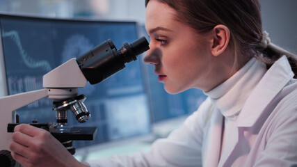 Female doctor working in laboratory. Using microscope, sitting behind monitor