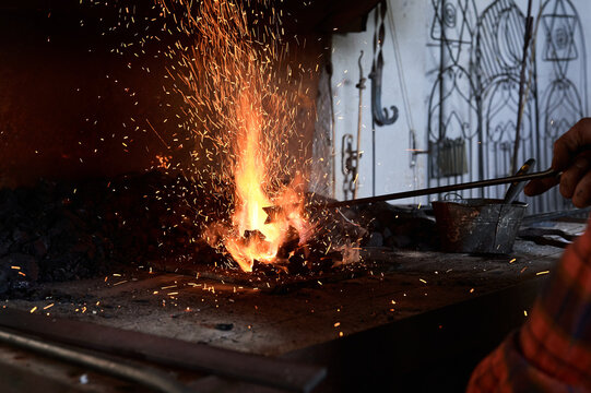 Crop unrecognizable male blacksmith heating metal rod on burning flame during forging process in workshop