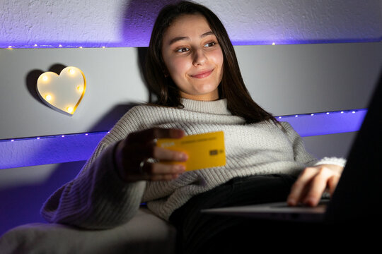 Side view teen in sweater typing credit card data on keyboard of netbook while shopping online