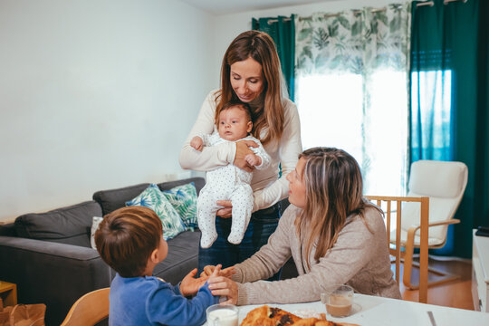 Cheerful homosexual woman with small baby standing near table with girlfriend and son while having meal