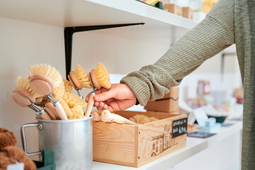 Crop anonymous female client taking wooden brush from container while shopping in zero waste shop