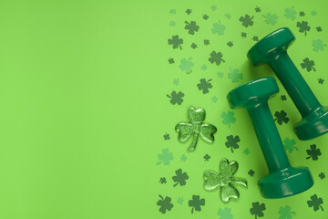 Two heavy dumbbells and Irish shamrock leaf clover. Healthy fitness gym flat lay composition...