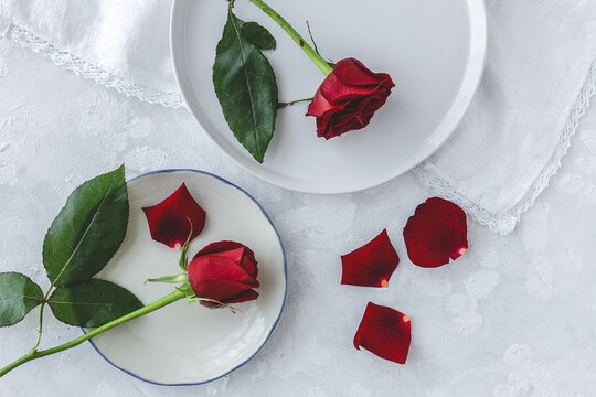 Top view of fresh red rose flowers and petals placed on table with plates and white cloth