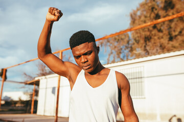Masculine ethnic male protester in undershirt standing with raised arm in countryside