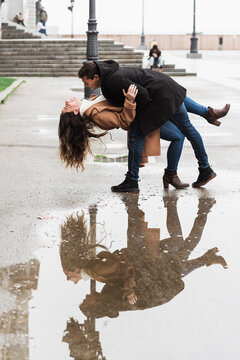 Side view full body joyful young couple in warm clothes dancing happily while woman bending backwards on sidewalk on street