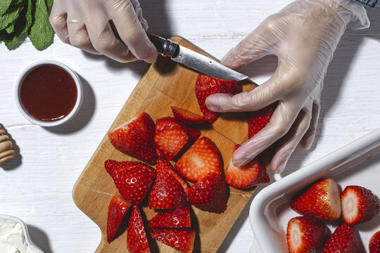 Top view crop unrecognizable chef in latex gloves cutting fresh delicious strawberries on wooden cutting board on table - Powered by Adobe